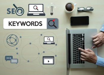 A tabletop view of a SEO team member's desk shows icons representing SEO, keywords, and a man's hands on a laptop. The man is writing about how keyword research can skyrocket SEO rankings and transform an enterprise's SEO strategy. The image shows that keyword research is an essential part of any successful SEO campaign.